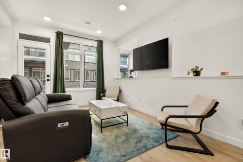 Recessed ceiling lighting, large windows with white trim, a glass-paned door, wood-finish flooring, and a wall-mounted display shelf - #53 16231 19 Av Sw, Edmonton, AB - Indoor