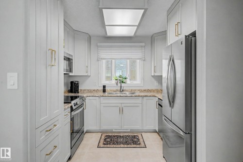 Galley kitchen featuring light-toned cabinetry, stainless steel appliances, granite-style countertops, and a window above the sink - 193 Kiniski Crescent Nw, Edmonton, AB - Indoor Photo Showing Kitchen With Upgraded Kitchen