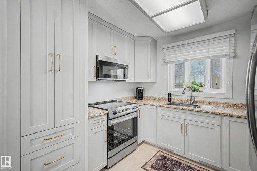 Light-toned cabinetry with gold-finish hardware, stainless steel appliances, speckled stone-look countertops, and a stainless steel sink with a gooseneck faucet - 193 Kiniski Crescent Nw, Edmonton, AB - Indoor Photo Showing Kitchen