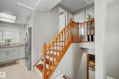 Wood staircase with turned balusters, light gray cabinetry, stainless steel refrigerator, and tiled flooring - 193 Kiniski Crescent Nw, Edmonton, AB - Indoor