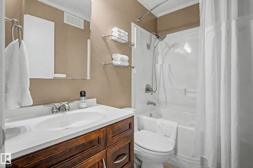 Bathroom featuring a dark wood-finish vanity with a white countertop and integrated sink, a mirrored medicine cabinet, a full bathtub with an overhead shower fixture, and a white shower curtain - 193 Kiniski Crescent Nw, Edmonton, AB - Indoor Photo Showing Bathroom