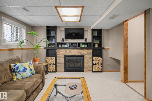 Stone-clad fireplace with a black metal insert, flanked by built-in shelving and wood storage - 193 Kiniski Crescent Nw, Edmonton, AB - Indoor With Fireplace