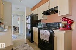 Galley-style kitchen featuring light-toned cabinetry, a black range with an overhead hood, a black refrigerator, and a stainless steel sink - 