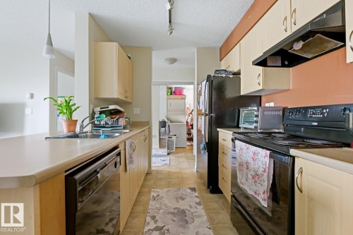 Kitchen featuring light-toned cabinetry, a double basin stainless steel sink, black appliances, and pendant lighting - #106 13907 136 St Nw, Edmonton, AB - Indoor Photo Showing Kitchen