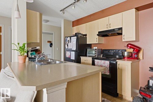 Kitchen featuring light-toned cabinetry, a stainless steel sink, black appliances, and track lighting - #106 13907 136 St Nw, Edmonton, AB - Indoor Photo Showing Kitchen With Double Sink