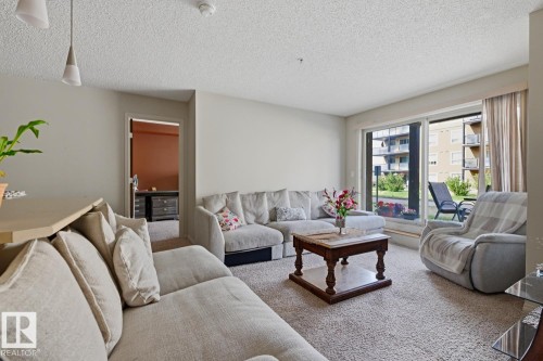 Sliding glass doors, textured carpet, and neutral wall tones - #106 13907 136 St Nw, Edmonton, AB - Indoor Photo Showing Living Room