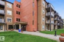 Multi-story building featuring a brick and stucco facade, glass-paneled balconies, and a concrete walkway - #106 13907 136 St Nw, Edmonton, AB  - Outdoor With Exterior 