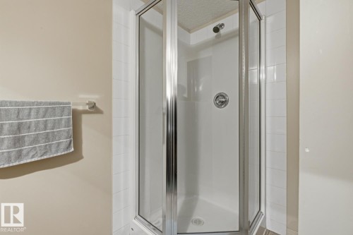 Corner shower enclosure with clear glass panels, chrome hardware, and white tile surround - #106 13907 136 St Nw, Edmonton, AB - Indoor Photo Showing Bathroom
