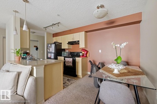 Kitchen featuring light-toned cabinetry, a double basin stainless steel sink, black appliances, and pendant lighting - #106 13907 136 St Nw, Edmonton, AB - Indoor