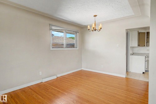 Hardwood flooring, classic chandelier, window with natural light, textured tray ceiling, and crown molding - 9723 76 Street Nw, Edmonton, AB - Indoor Photo Showing Other Room