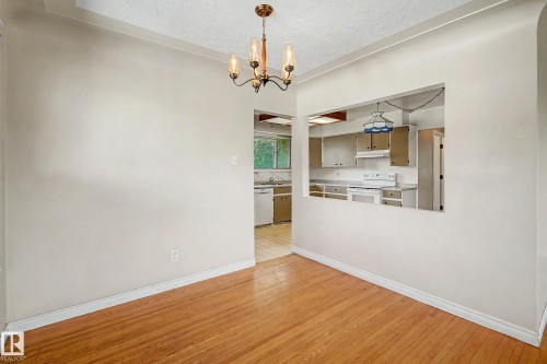 Wood-finish flooring, overhead chandelier, and a kitchen pass-through window with an integrated pendant light - 9723 76 Street Nw, Edmonton, AB - Indoor Photo Showing Kitchen