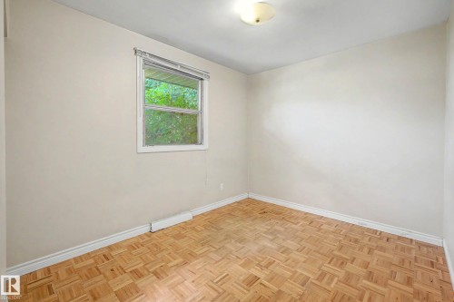 Parquet wood-finish flooring with perimeter baseboard, single window with blinds, and flush-mount ceiling light - 9723 76 Street Nw, Edmonton, AB - Indoor Photo Showing Other Room