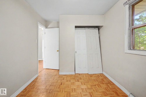 Wood-finish parquet flooring, white interior doors, and a window with white trim - 9723 76 Street Nw, Edmonton, AB - Indoor Photo Showing Other Room