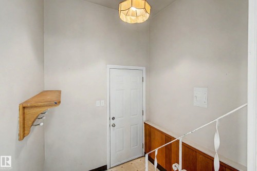 White paneled door, decorative wood-finish wall paneling, and a white metal handrail - 9723 76 Street Nw, Edmonton, AB - Indoor Photo Showing Other Room
