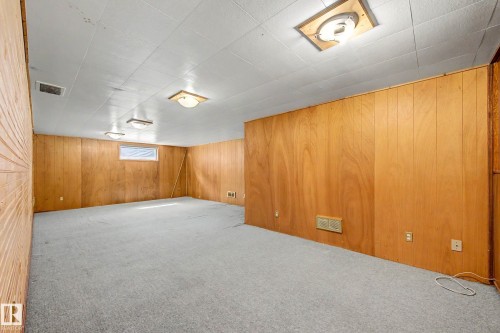 Spacious room featuring wood paneling, light gray carpeting, a drop ceiling, and multiple flush-mount light fixtures - 9723 76 Street Nw, Edmonton, AB - Indoor