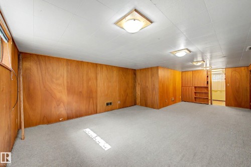 Spacious room featuring wood paneling, built-in cabinetry, and neutral carpeting - 9723 76 Street Nw, Edmonton, AB - Indoor