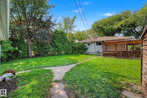 Expansive backyard featuring a lush lawn, mature trees, concrete pathway, and a covered wood deck - 9723 76 Street Nw, Edmonton, AB - Outdoor