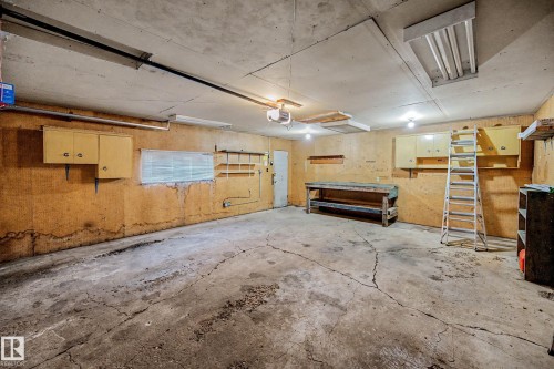 Spacious garage featuring concrete flooring, built-in cabinetry, an integrated workbench, and overhead lighting fixtures - 9723 76 Street Nw, Edmonton, AB - Indoor Photo Showing Garage