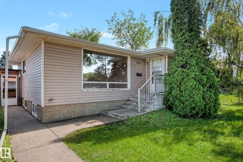Siding exterior with a large picture window, concrete walkway, established lawn, and mature landscaping - 9723 76 Street Nw, Edmonton, AB - Outdoor