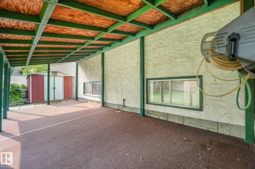 Covered patio featuring an exposed plywood ceiling with green structural beams, a textured exterior wall, and a patterned paver floor - 4135 134 Avenue Nw, Edmonton, AB - Outdoor With Exterior