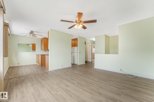 Expansive living area featuring wood-finish flooring, two ceiling fans, and a partial wall separating spaces - 4135 134 Avenue Nw, Edmonton, AB - Indoor
