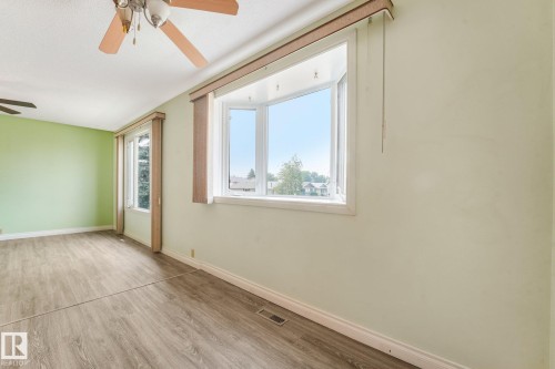 Spacious room featuring a bay window, two standard windows, wood-finish flooring, light green wall paint, and a ceiling fan - 4135 134 Avenue Nw, Edmonton, AB - Indoor Photo Showing Other Room