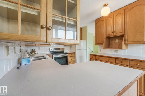 Kitchen featuring wood cabinetry, white tiled backsplash, stainless steel sink, and light-toned countertops - 4135 134 Avenue Nw, Edmonton, AB - Indoor Photo Showing Kitchen With Double Sink
