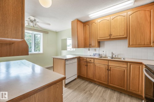 Kitchen featuring wood cabinetry, light countertops, white tile backsplash, and wood-finish flooring - 4135 134 Avenue Nw, Edmonton, AB - Indoor Photo Showing Kitchen With Double Sink