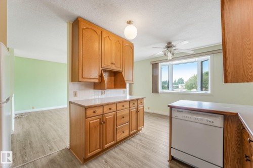 Kitchen featuring wood cabinetry, white tile backsplash, light-toned countertops, and wood-finish flooring - 4135 134 Avenue Nw, Edmonton, AB - Indoor Photo Showing Kitchen