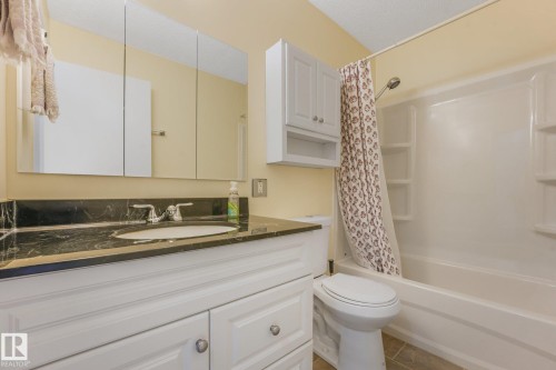 Bathroom featuring a white vanity with paneling, dark stone countertop, and an undermount sink - 4135 134 Avenue Nw, Edmonton, AB - Indoor Photo Showing Bathroom
