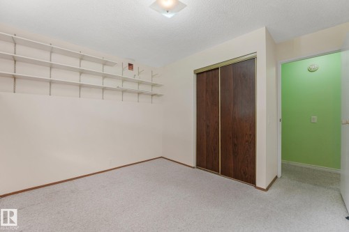 Carpeted room featuring a ceiling-mounted light fixture, extensive wall-mounted shelving, wood-paneled sliding closet doors, and light-toned walls - 4135 134 Avenue Nw, Edmonton, AB - Indoor Photo Showing Other Room