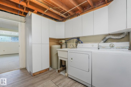 Dedicated utility space featuring extensive white cabinetry, a utility sink, and wood-finish flooring - 4135 134 Avenue Nw, Edmonton, AB - Indoor Photo Showing Laundry Room
