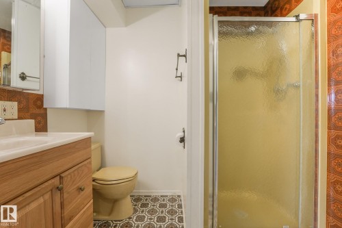 Bathroom featuring a wood-finish vanity with an integrated sink, patterned floor tiling, and a separate shower enclosure with frosted glass - 4135 134 Avenue Nw, Edmonton, AB - Indoor Photo Showing Bathroom