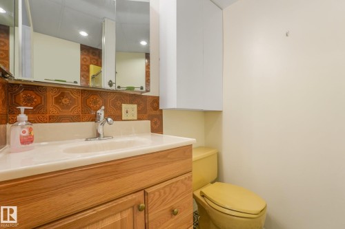 Bathroom featuring a wood-finish vanity with a built-in sink, a wall-mounted medicine cabinet with mirror, patterned backsplash tiling, a wall-mounted storage cabinet, and a toilet - 4135 134 Avenue Nw, Edmonton, AB - Indoor Photo Showing Bathroom