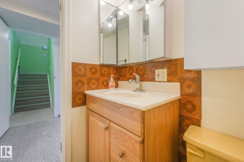 Bathroom vanity with light wood-finish cabinetry, integrated sink, and an ornamental tiled backsplash - 4135 134 Avenue Nw, Edmonton, AB - Indoor Photo Showing Bathroom