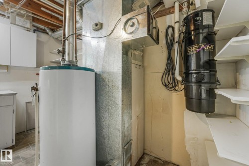 Utility area featuring a water heater, central vacuum system, exposed ceiling joists, and a combination of closed and open shelving - 4135 134 Avenue Nw, Edmonton, AB - Indoor Photo Showing Basement