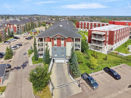 Multi-story building featuring balconies, a sloped driveway to underground parking, and surrounding green spaces - #205 5816 Mullen Pl Nw, Edmonton, AB - Outdoor With Balcony With View