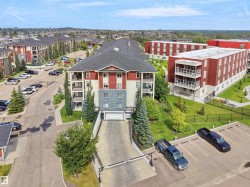 Multi-story building featuring balconies, a sloped driveway to underground parking, and surrounding green spaces - 