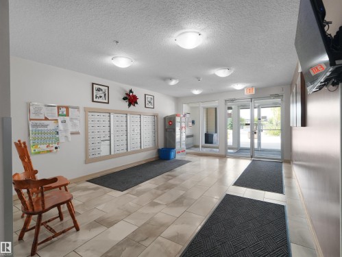 Tiled flooring leading to an exterior glass door, with built-in mailboxes and overhead lighting - #205 5816 Mullen Pl Nw, Edmonton, AB - Indoor Photo Showing Other Room