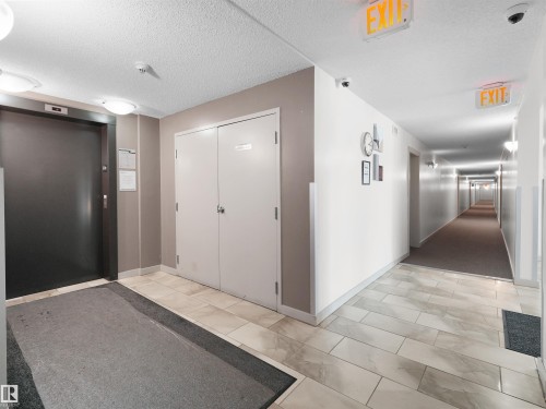 Elevator access, tile flooring, flush-mounted ceiling lights, and hallway with wall sconces - #205 5816 Mullen Pl Nw, Edmonton, AB - Indoor Photo Showing Other Room