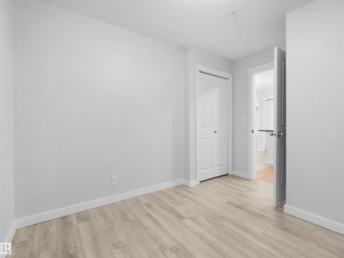 Light wood-finish flooring, white walls, and a bi-fold closet door - #205 5816 Mullen Pl Nw, Edmonton, AB - Indoor Photo Showing Other Room