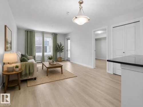 Recessed lighting, wood-finish flooring, white trim, and a white interior door with dark hardware - #205 5816 Mullen Pl Nw, Edmonton, AB - Indoor Photo Showing Living Room