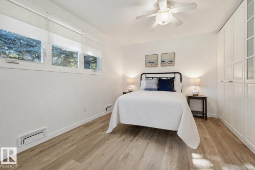 Wood-finish flooring, white walls, built-in cabinetry, multiple windows, and a ceiling fan with integrated lighting - 9127 149 Street Nw, Edmonton, AB - Indoor Photo Showing Bedroom