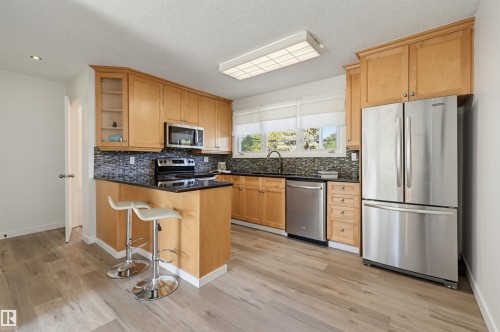 Kitchen featuring wood-finish flooring, natural wood cabinetry, black countertops, stainless steel appliances, and a tiled backsplash - 9127 149 Street Nw, Edmonton, AB - Indoor Photo Showing Kitchen