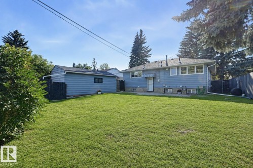 Expansive grassy backyard featuring a detached garage with siding, mature trees, and a wooden fence - 9127 149 Street Nw, Edmonton, AB - Outdoor