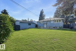 Expansive grassy backyard featuring a detached garage with siding, mature trees, and a wooden fence - 