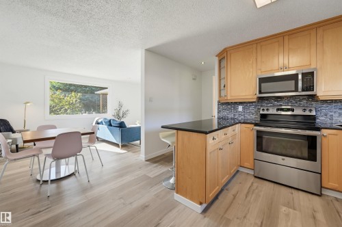 Stainless steel appliances, wood-finish flooring, light wood cabinetry, dark countertop, and mosaic tile backsplash - 9127 149 Street Nw, Edmonton, AB - Indoor Photo Showing Kitchen