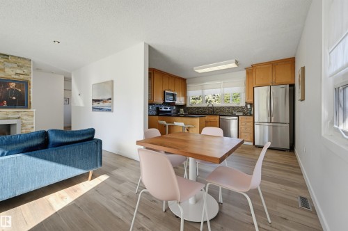 Wood-finish flooring throughout, stacked stone fireplace, stainless steel kitchen appliances, kitchen cabinetry with ample storage, and multiple windows - 9127 149 Street Nw, Edmonton, AB - Indoor