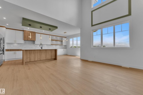 Open concept living space featuring wood-finish flooring, white cabinetry, a large kitchen island with wood-finish paneling, and multiple large windows - 764 Astoria Way, Devon, AB - Indoor Photo Showing Kitchen