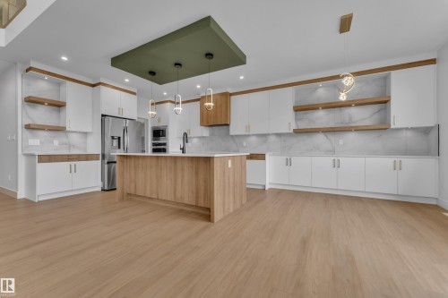 Light wood-finish flooring, white cabinetry with gold-toned hardware, center island with light countertop, built-in stainless steel appliances, and decorative suspended light fixtures - 764 Astoria Way, Devon, AB - Indoor Photo Showing Kitchen With Upgraded Kitchen